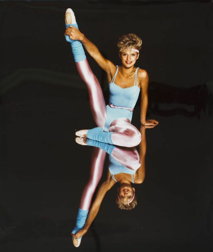 80s fashion trends, smiling blonde woman with short hair, wearing light pastel blue body suit and legwarmers, shiny pink leggings belt and headband