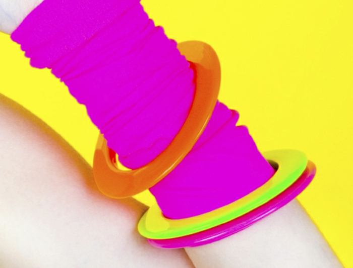 close up of arm with a neon pink arm-warmer, neon orange yellow and pink bangles, acid yellow background