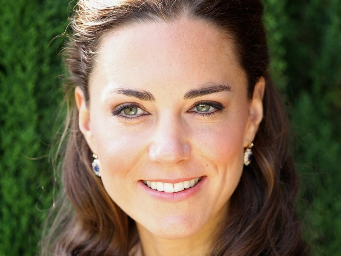 close up of kate middleton, natural brown wavy hair, tied back at the top, smile and green eyes, natural looking make-up, earrings with blue gems