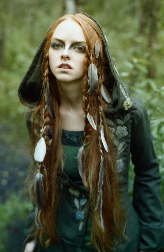 medieval braids, young woman wearing green embroidered dress with hood, long ginger hair, decorated with several braids, and many feathers, strong green eye makeup