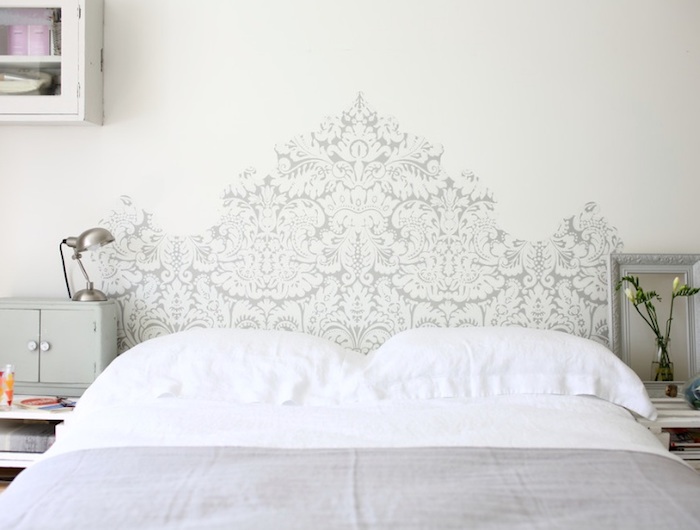 headboard-like decoration, in baroque style, painted in pale gray behind a double bed, wall art décor, small vase with white flowers, silver bedside lamp