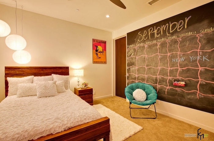 blackboard with calendar for september, drawn in yellow and pink chalk, on bedroom wall, near teal chair and wooden bed