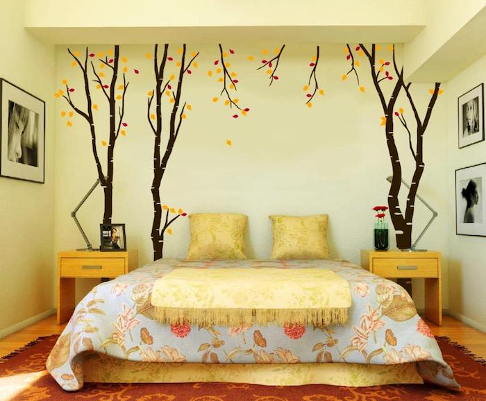 autumn trees with yellow and red leaves, painted on a pale yellow wall, creative wall decor ideas, near a double bed with floral covers, yellow tasseled throw, and two matching cushions