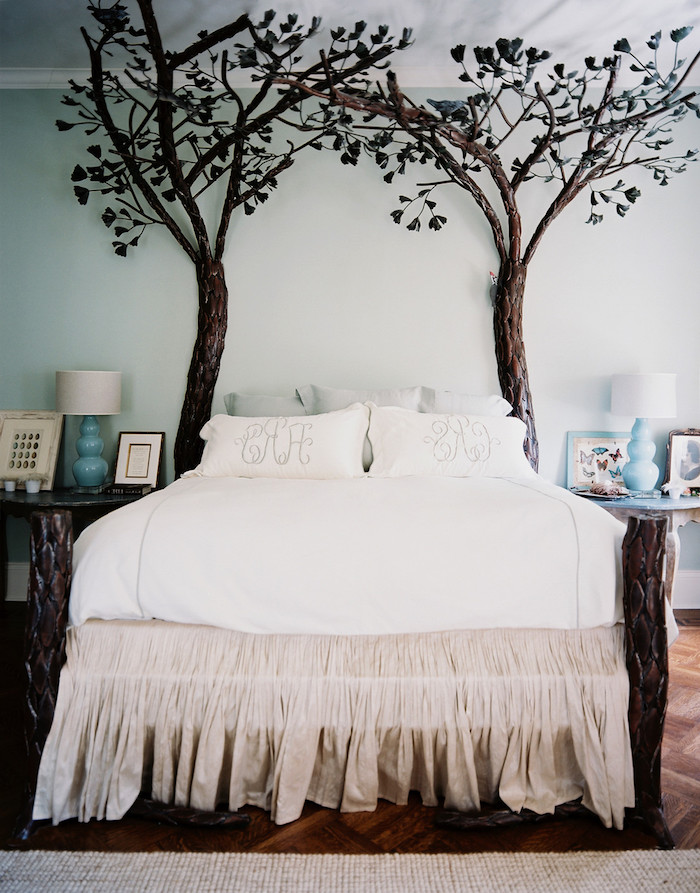 dark brown fake trees, with dark green leaves, wall art décor, placed on witer side of a bed, with white and pale beige covers and pillows