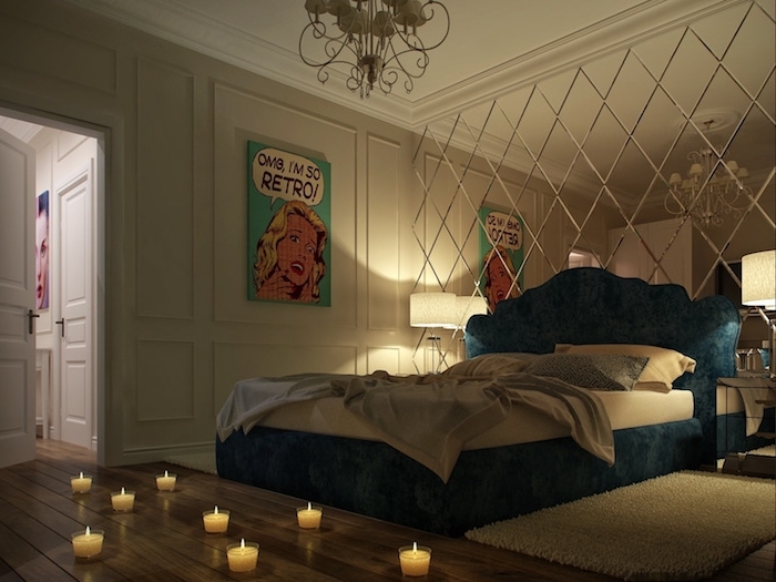 eight small lit candles, on a wooden floor, near blue bed with soft headboard, one wall features white paneling and pop art poster, the other is covered by mirror in diamond shapes