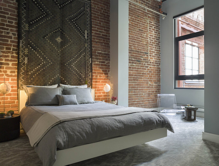big dark gray rectangular rug, with white and black details, hanging on a brick wall, over a double bed, with grey pillows and covers, bedroom design, industrial style room