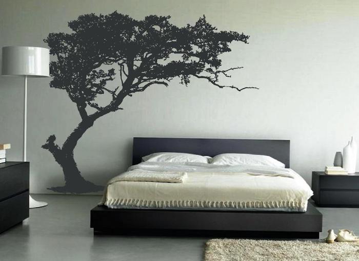 silhouette of a tree, painted in black on a pale gray wall, large wall art, near black bed with matching cupboards, pale gray lamp, beige fluffy rug