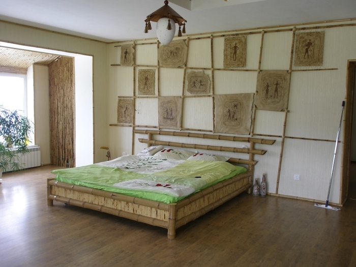 parchment pieces in beige, covered in brown tribal drawings, hung on bamboo poles, on a cream wall, near asian-inspired bamboo bed
