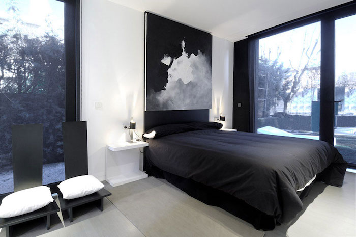 black and white bedroom design, with white walls, two black chairs with white cushions, black bed and window frames, large artwork in gray, black and white