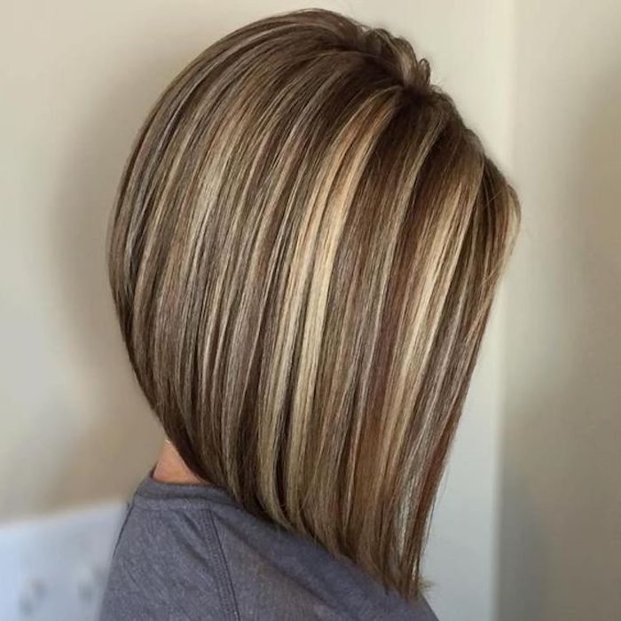asymmetrical straight bob, on medium brown hair, with light blonde contrasting highlights, worn by woman in grey top