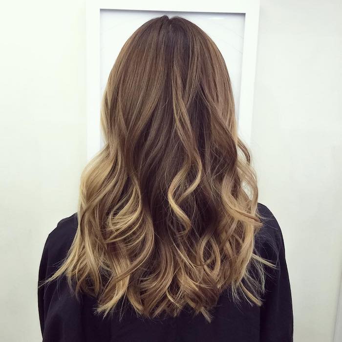 white door and off-white wall, faced by woman with medium length wavy hair, dark blonde balayage brown hair, black long-sleeved top