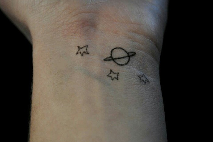 planet with a ring, and three stars, simple but cool arm tattoos, inspired by antoine de saint-exupéry's classic, le petit prince, on a person's wrist