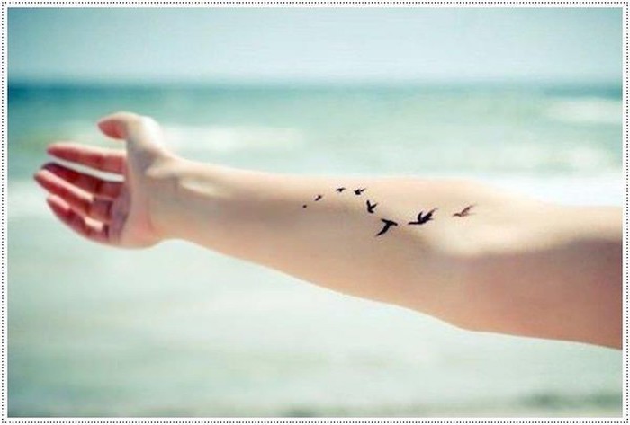 arm in the air, birds tattoo on the forearm, meaningful tattoo ideas, ocean waves in the background