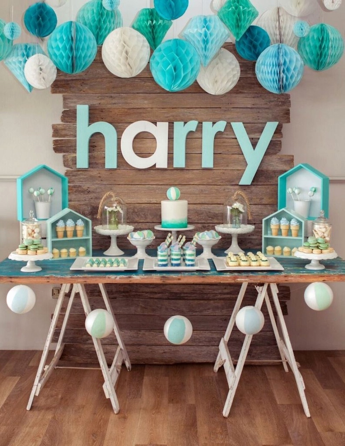 white blue and turquoise paper flowers hanging, baby shower centerpieces boy, cake and sweets on the table