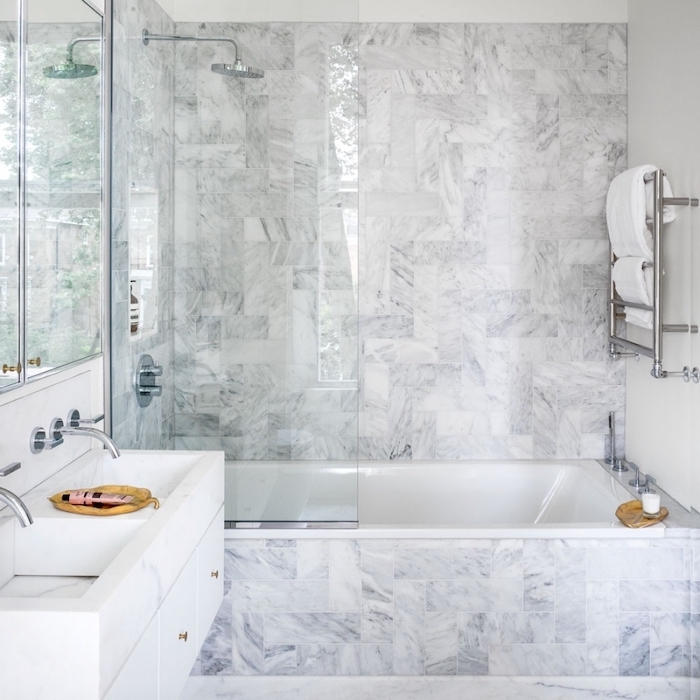 marble tiled walls and bathtub, glass shower door, small bathroom layout, floating white cabinets and sink
