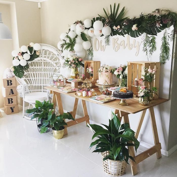 greenery and white balloons hanging, baby shower themes for boys, wooden crates with flowers, sweets on the table