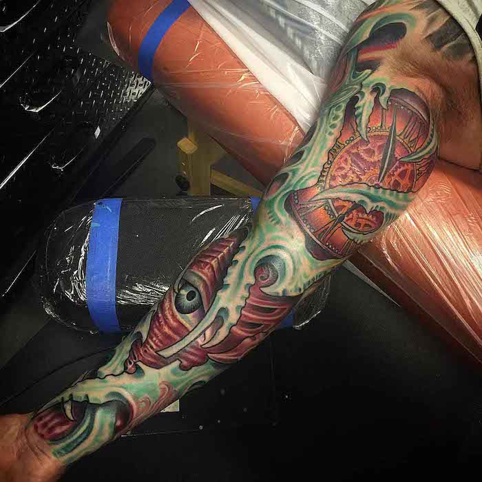 intricate coloured, arm sleeve tattoo, sleeve tattoos for men, hand resting on a black chair