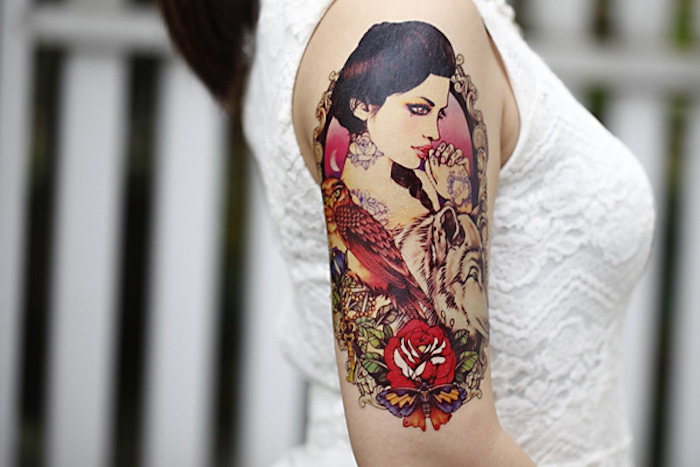 woman wearing a white top, meaningful tattoos, woman with wolf and bird, lots of flowers, shoulder tattoo