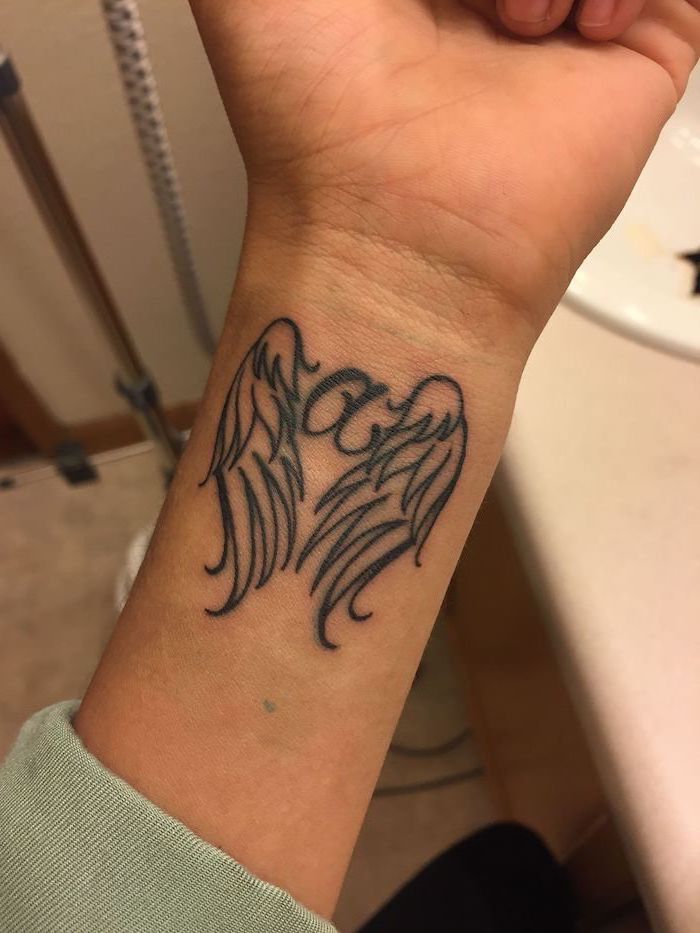 wrist tattoo, letter a, between two angel wings, angel sleeve tattoo, blurred background