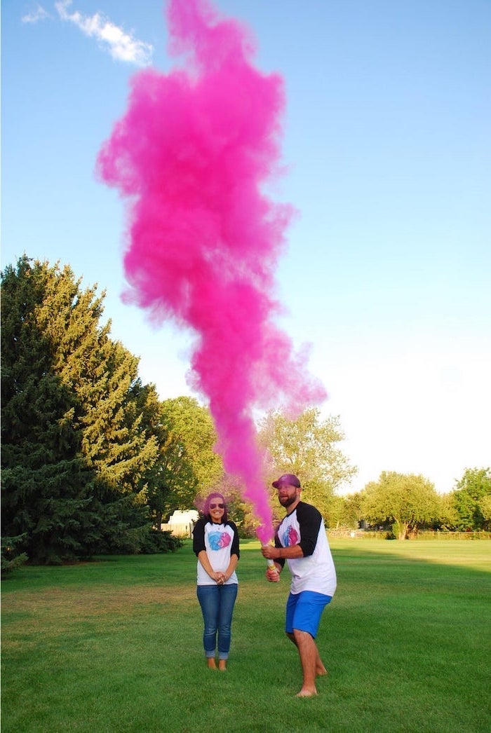 man and woman, standing in a field, man holding, pink smoke bomb, gender reveal ideas