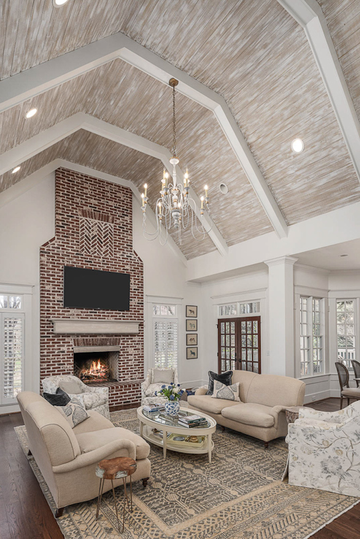 brick fireplace wall, vaulted ceiling ideas, white sofas, wooden floor, throw pillows, hanging chandelier