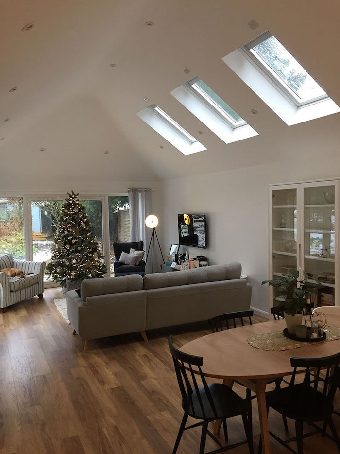 white ceiling with skylights, grey sofa, christmas tree, what is a vaulted ceiling, wooden floor, wooden table