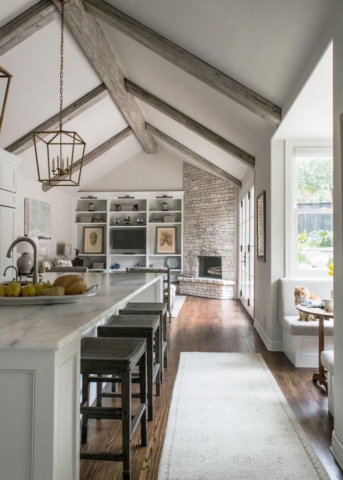stone fireplace wall, marble kitchen island, what is a vaulted ceiling, wooden floor, grey wooden beams
