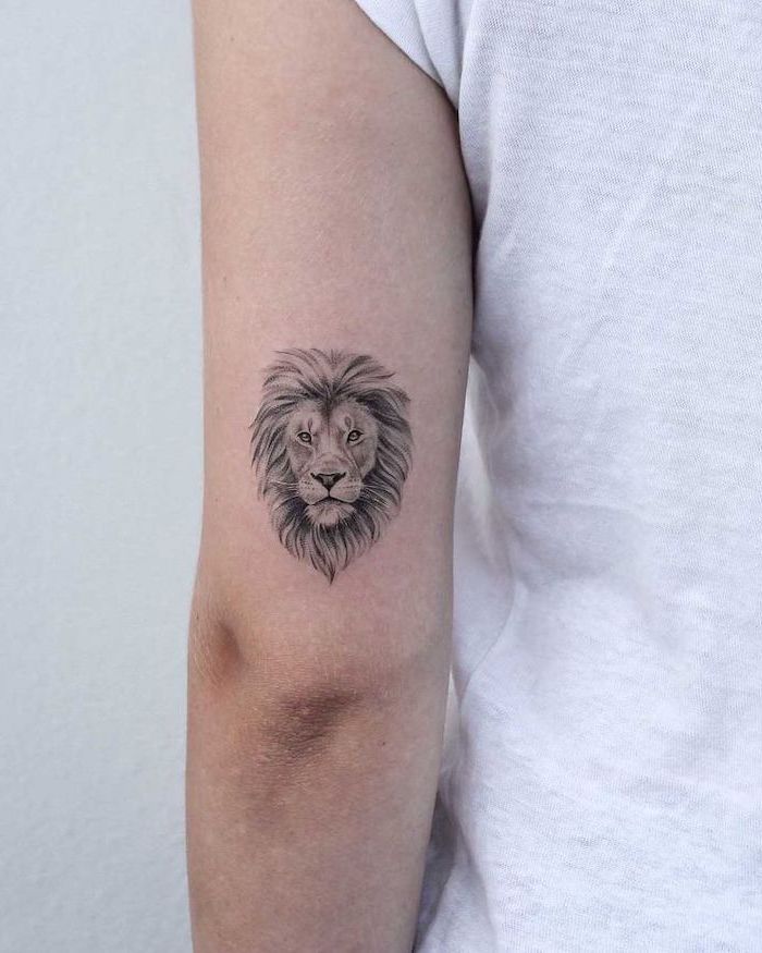 lion tattoo, back of arm tattoo, small lion head with mane, tattoo on woman wearing white t shirt