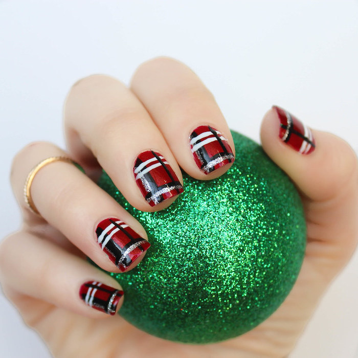hand holding a green bauble, nail colors, plaid decorations on each nail, done with red black white and gold nail polish