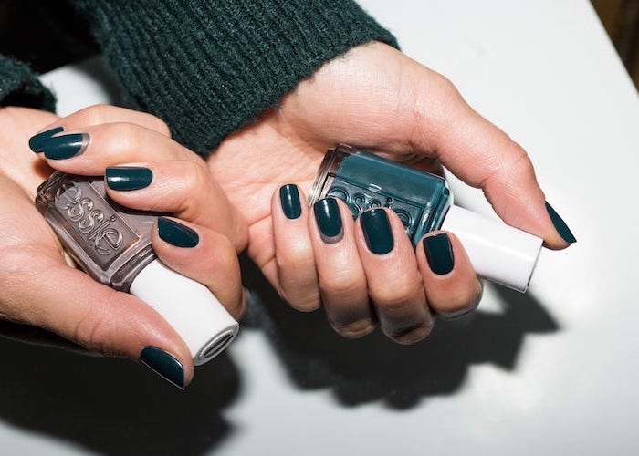 dark green nail polish on short squoval nails, neutral nail colors, two hands holding two different nail polish bottles