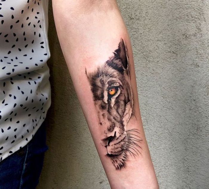half of a lioness head with yellow eyes, forearm tattoo on woman, wearing jeans and white top, lion chest tattoo