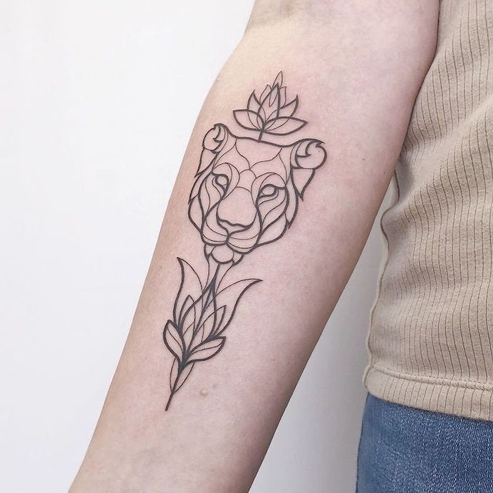 lion king tattoo, forearm tattoo, on woman wearing jeans and beige top, geometrical contoured lion head with lotus flowers