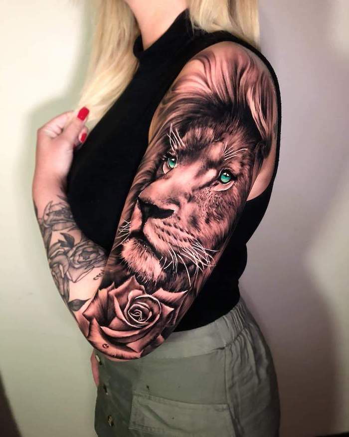 sleeve tattoo, on woman with blonde hair, wearing khaki pants and black top, lion with crown tattoo, lion head with blue eyes