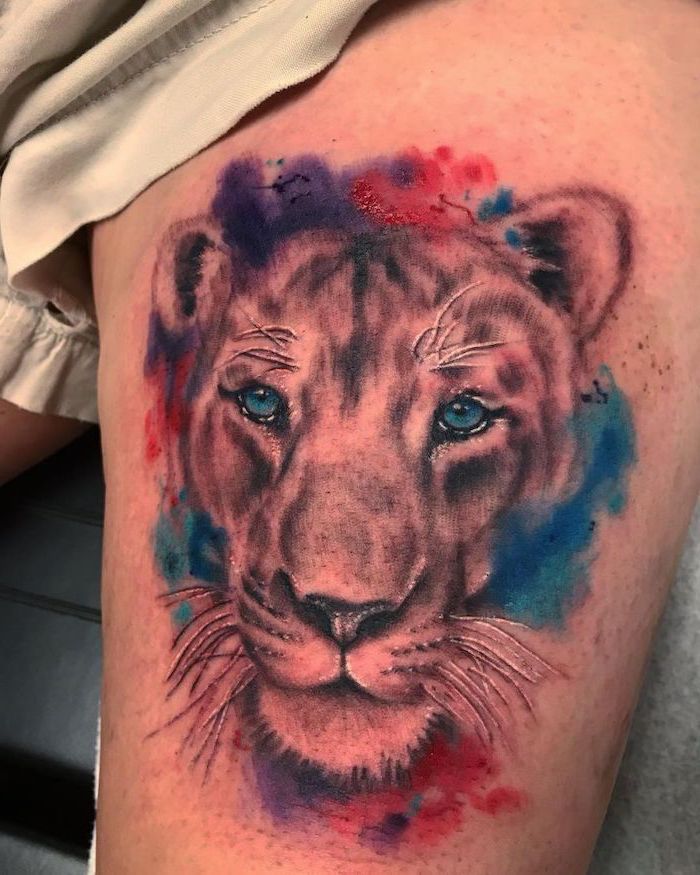 watercolor tattoo, lion thigh tattoo, lioness head with blue eyes, surrounded by different colors