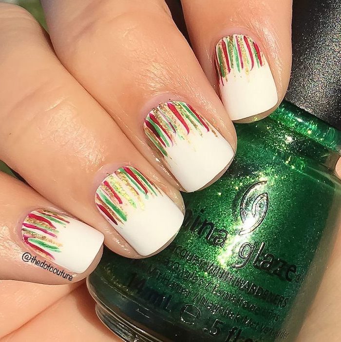 winter acrylic nails, hand holding nail polish bottle, white nail polish, red green and gold brush strokes