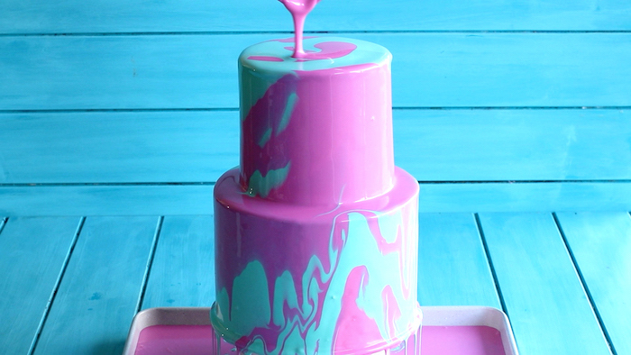 two tier cake, covered with blue and pink glaze, mirror glaze, placed on blue wooden background